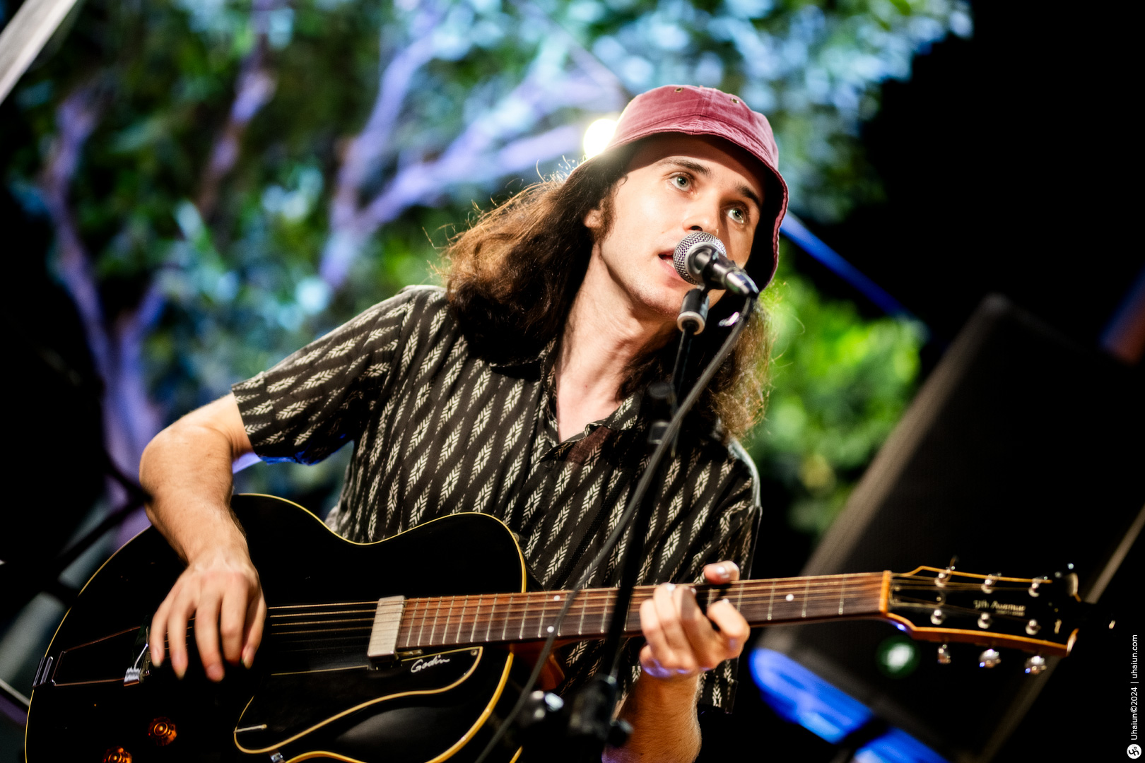 Guitarist singing on stage with microphone and trees