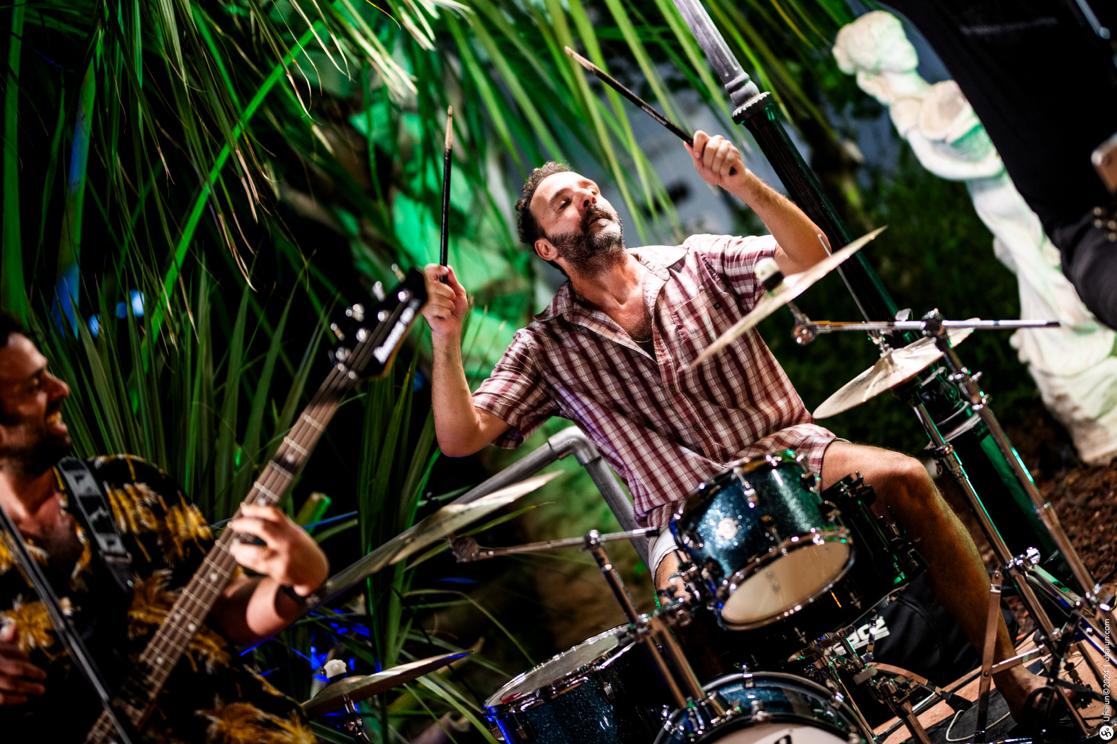 Drummer playing with band at outdoor night event.