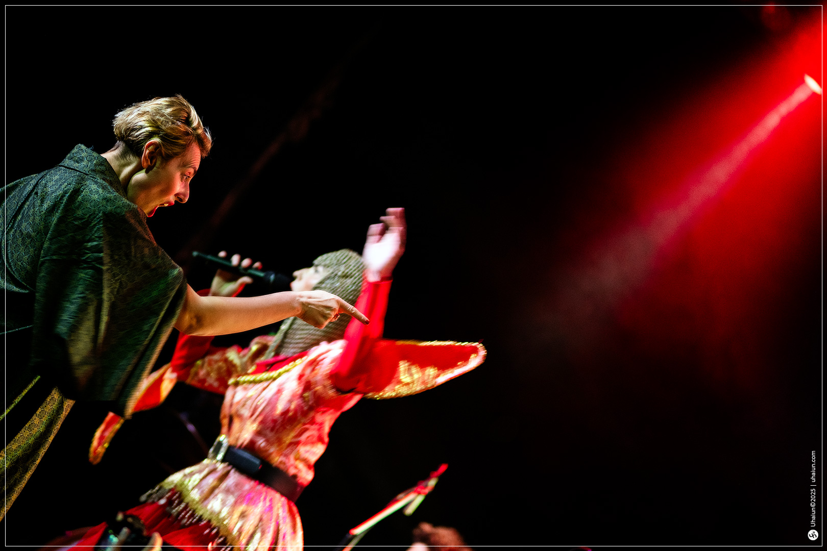 Two performers on stage under red lights