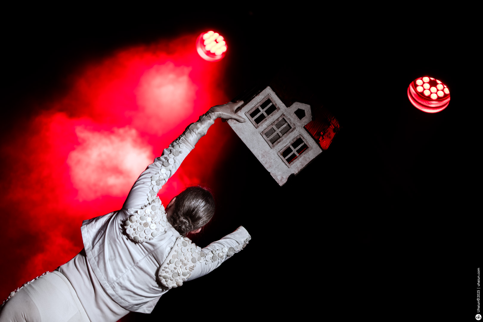Performer holds small house under red lights